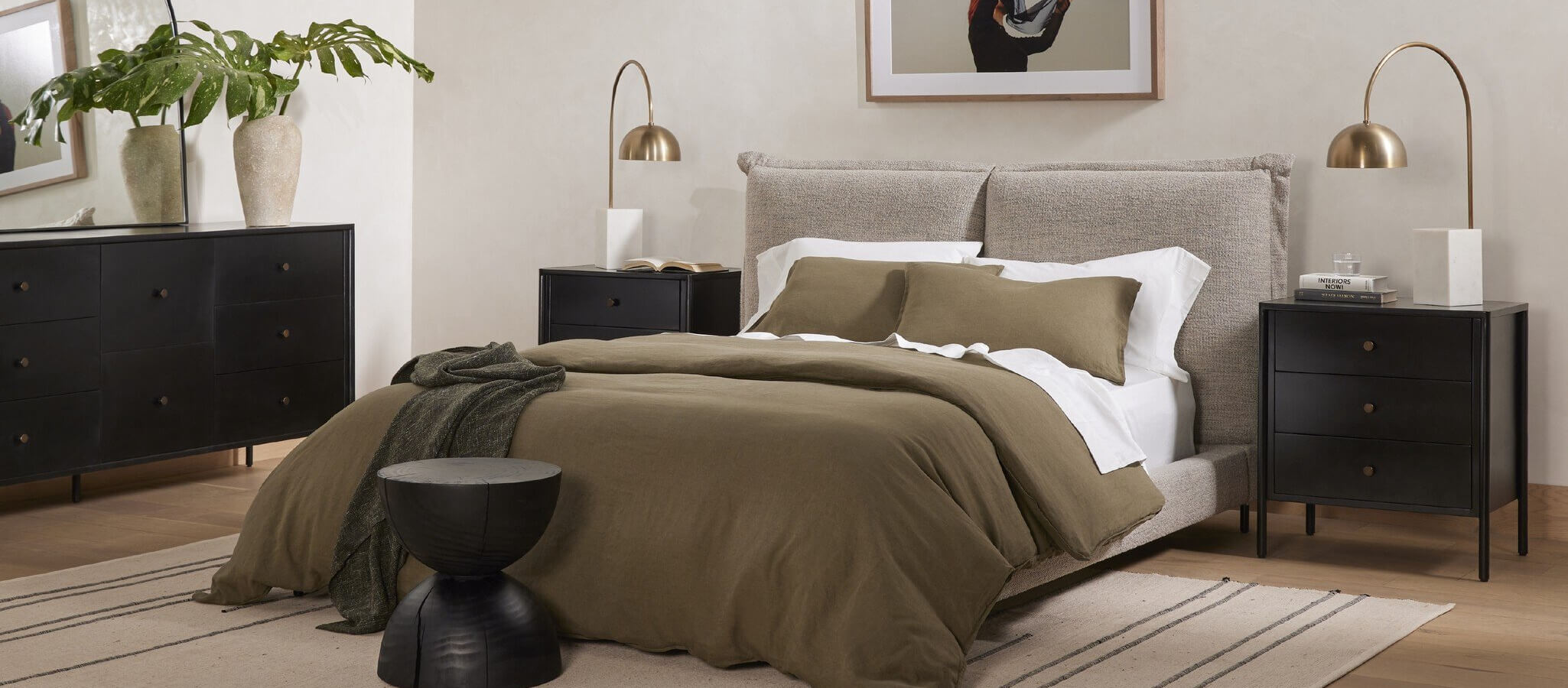Four Hands nightstands flank a bed with a plush grey headboard