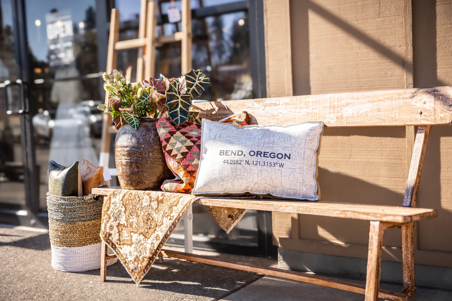 Wooden bench with decorative pillows and a plant on a sidewalk in Bend, Oregon.